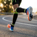 Gros plan sur les jambes d'un coureur portant des chaussures de running à plaque carbone sur une route en extérieur.
