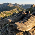 Paire de chaussures de trail Salomon boueuses posées sur un rocher face à une vue panoramique sur les montagnes.