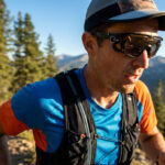 Un coureur de trail portant des lunettes de soleil de sport, une casquette et un sac d'hydratation en montagne.