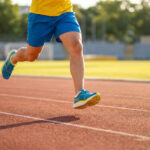 Coureur portant des baskets Asics Novablast 4 en pleine foulée sur une piste d'athlétisme.