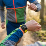 Coureuse regardant sa montre GPS jaune avec des données de course affichées pendant un entraînement en forêt.