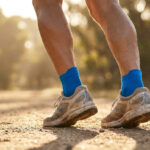 Gros plan sur les jambes d'un coureur avec des chaussures de trail usées et des chaussettes bleues sur un sentier.