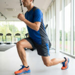 Un coureur en tenue de sport réalise une fente avant dans une salle de sport moderne avec vue sur une piste.