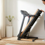 Un homme range un tapis de course pliable au design élégant en bois dans un salon lumineux.