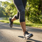 Une personne court sur une route ensoleillée en portant une genouillère de compression noire.
