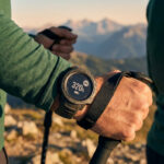 Un randonneur porte une montre Garmin Enduro 3 affichant 320h d'autonomie GPS avec les montagnes en arrière-plan.