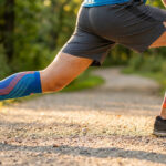 Coureur faisant des étirements sur un chemin avec des manchons de compression bleus et orange.