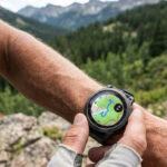 Coureur regardant une carte topographique sur sa montre GPS au poignet en montagne.