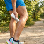 Un coureur applique une crème anti-frottement sur sa jambe sur un sentier en forêt.