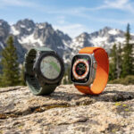 Garmin Fenix 8 et Apple Watch Ultra 2 posées sur un rocher avec en arrière-plan des montagnes enneigées.